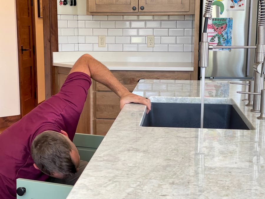 Hellgate plumber reaching underneath kitchen sink during a drain cleaning.